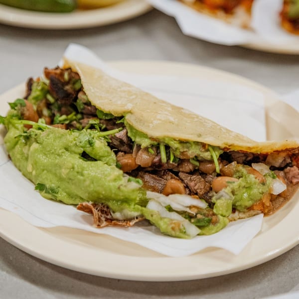 A Tacos El Franc taco filled with meat, beans, onions, and guacamole on a plate.