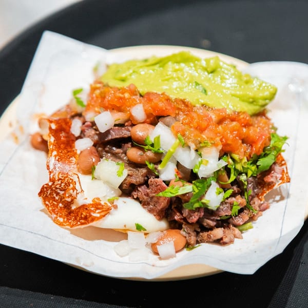 A Tacos El Franc taco with carne asada, beans, pico de gallo, guacamole, and cheese.