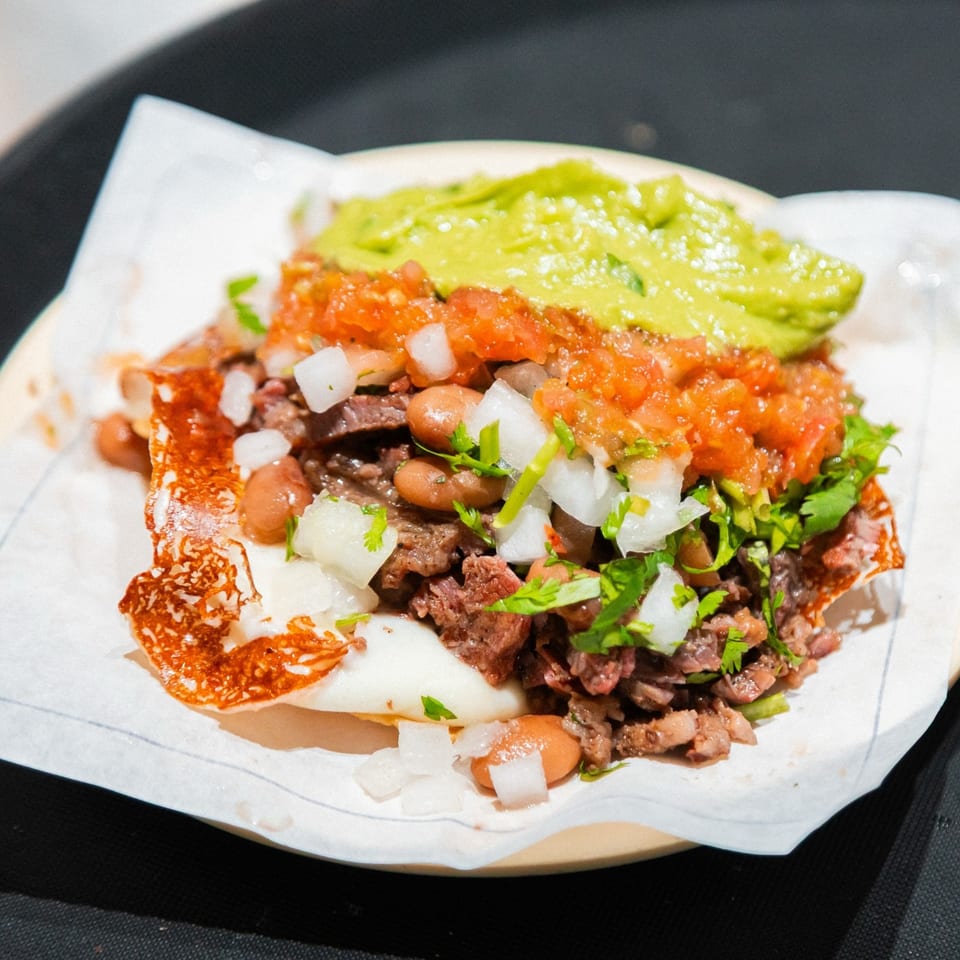 A Tacos El Franc taco with carne asada, beans, pico de gallo, guacamole, and cheese.
