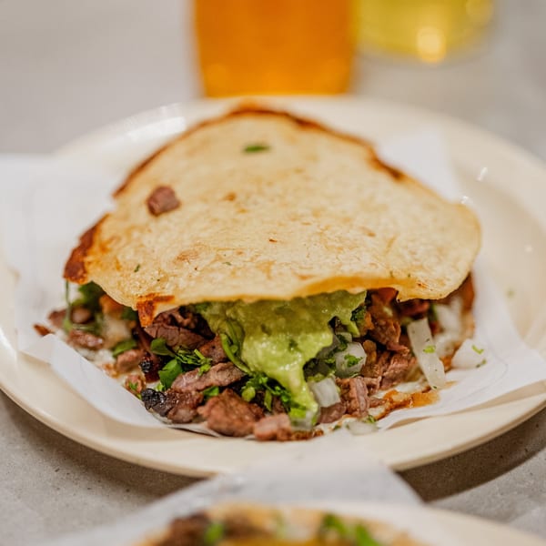 A Tacos El Franc taco with carne asada, guacamole, onions, and cilantro on a plate.