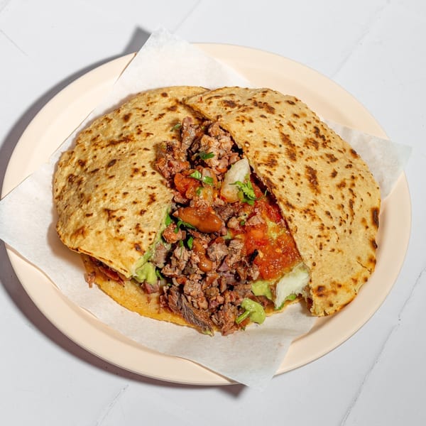 A large Tacos El Franc quesadilla, filled with carne asada, guacamole, salsa, and beans.