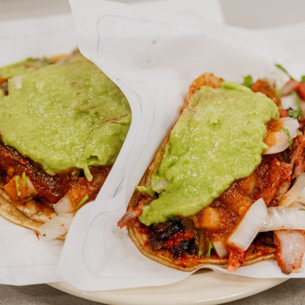 Two Tacos El Franc tacos with generous guacamole, red meat, and onions on a plate.