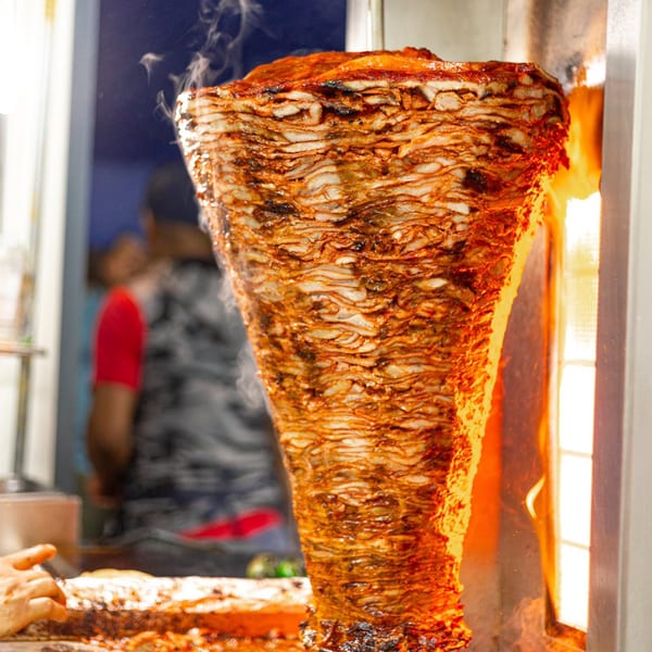 Vertical spit of sizzling al pastor meat cooking over an open flame at Tacos El Franc.