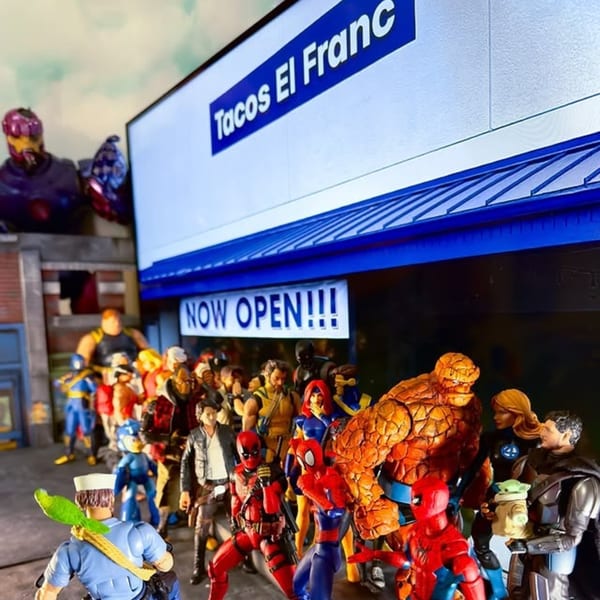 Superhero action figures line up outside Tacos El Franc, with a "NOW OPEN!!!" banner displayed.