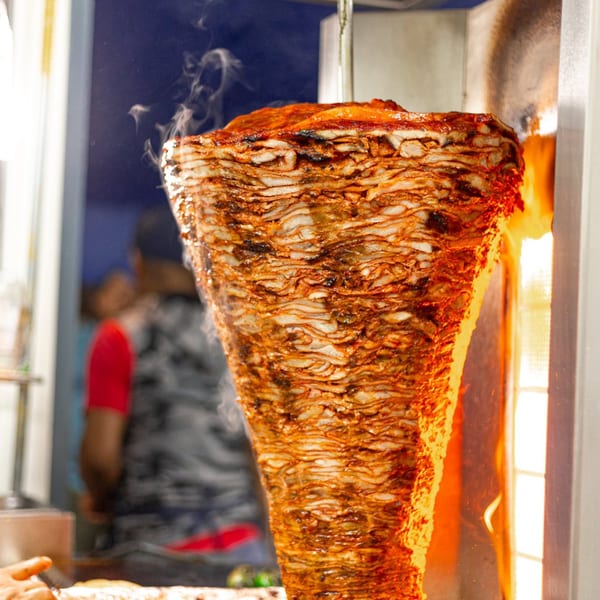 Vertical spit of sizzling al pastor meat cooking over an open flame at Tacos El Franc.