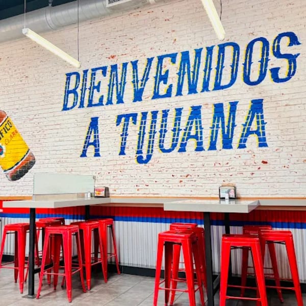 Tacos El Franc interior with "Bienvenidos a Tijuana" mural, red stools, and light gray tables.