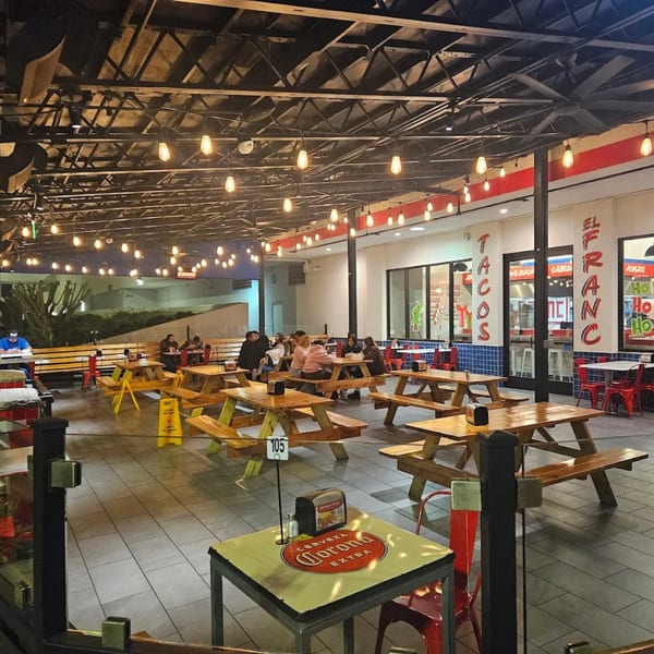 Tacos El Franc's outdoor dining area with picnic tables, string lights, and patrons enjoying tacos.