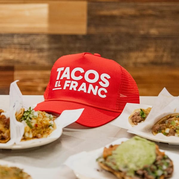 Red Tacos El Franc hat surrounded by several plates of tacos on a table.